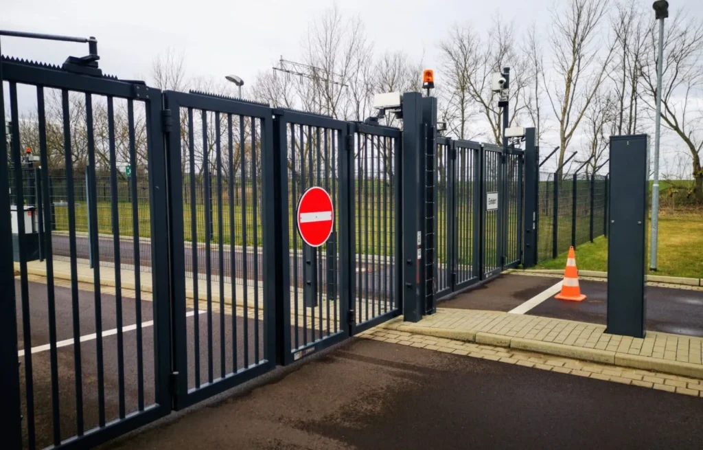 Black metal industrial security gate with vertical bars and a red stop sign at a commercial property entrance.