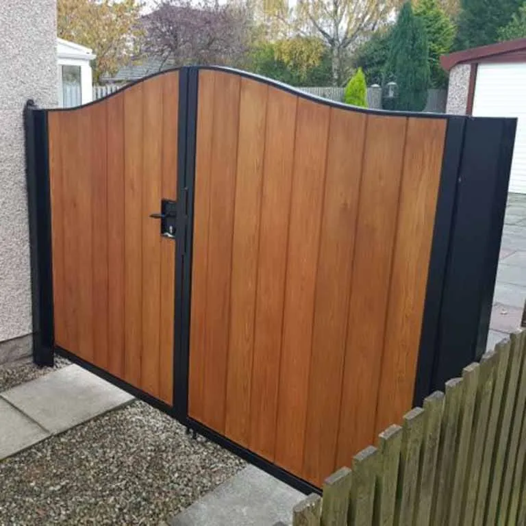 Wood grain metal pedestrian gate with black framing and a curved top installed beside a residential fence.