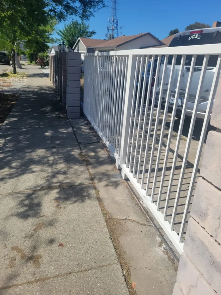 White metal vertical bar side gate installed along a sidewalk beside a residential property.
